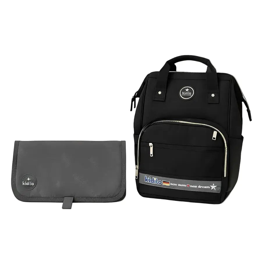 Kidilo black diaper backpack with smooth front pocket and printed logo strip, shown beside a grey changing mat.