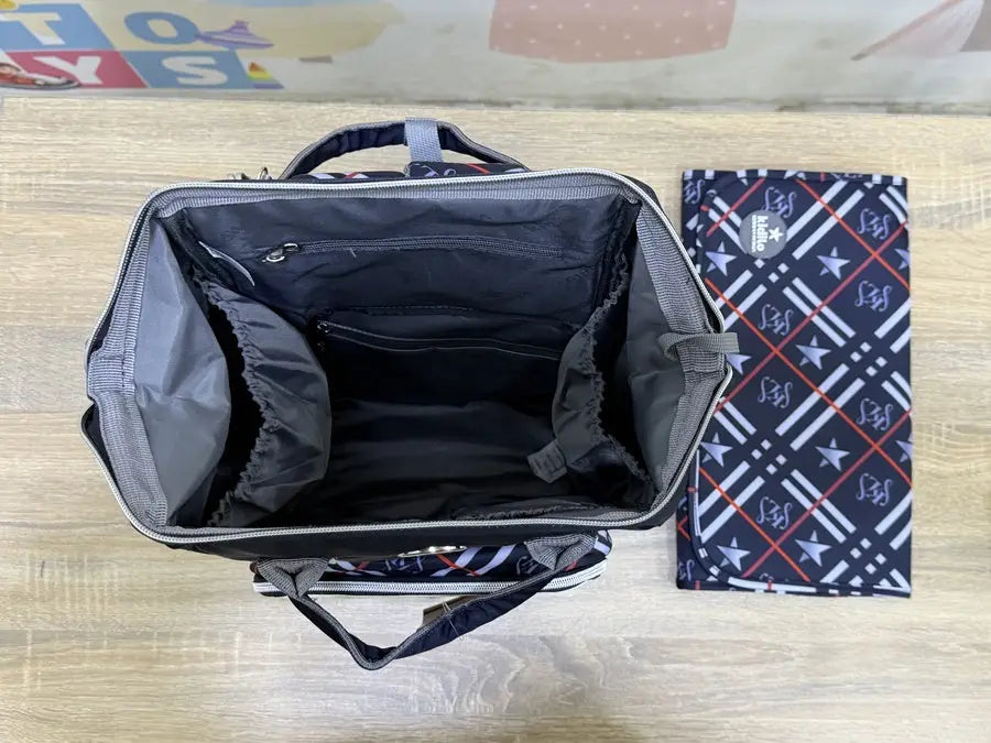 Kidilo Plaid-Print: black open compartment beside plaid changing mat on wooden surface.