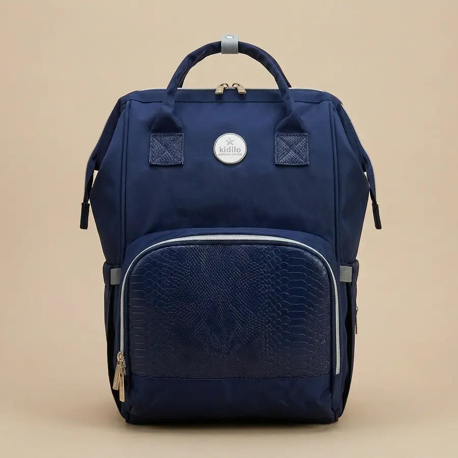 Kidilo blue diaper backpack photographed against a beige background, with textured front pocket and round logo patch.