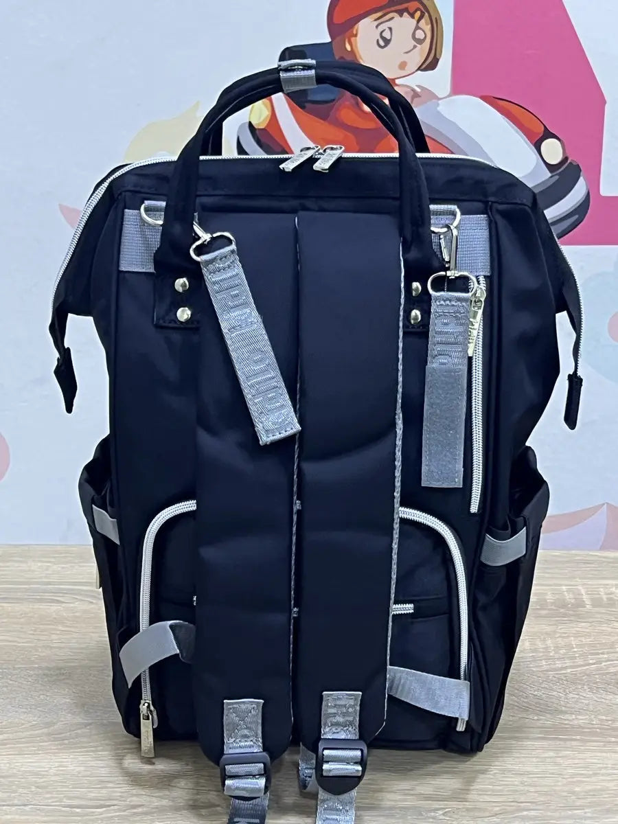 Kidilo dark blue diaper backpack rear view on a wooden surface, showing shoulder straps, grey clips and zip pocket.