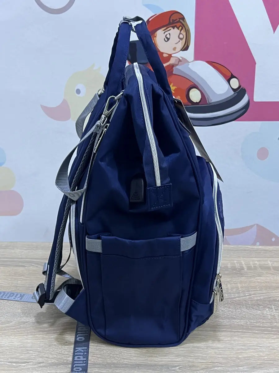 Kidilo blue diaper backpack side view on a wooden surface, with side pocket, grey loops and top handles.