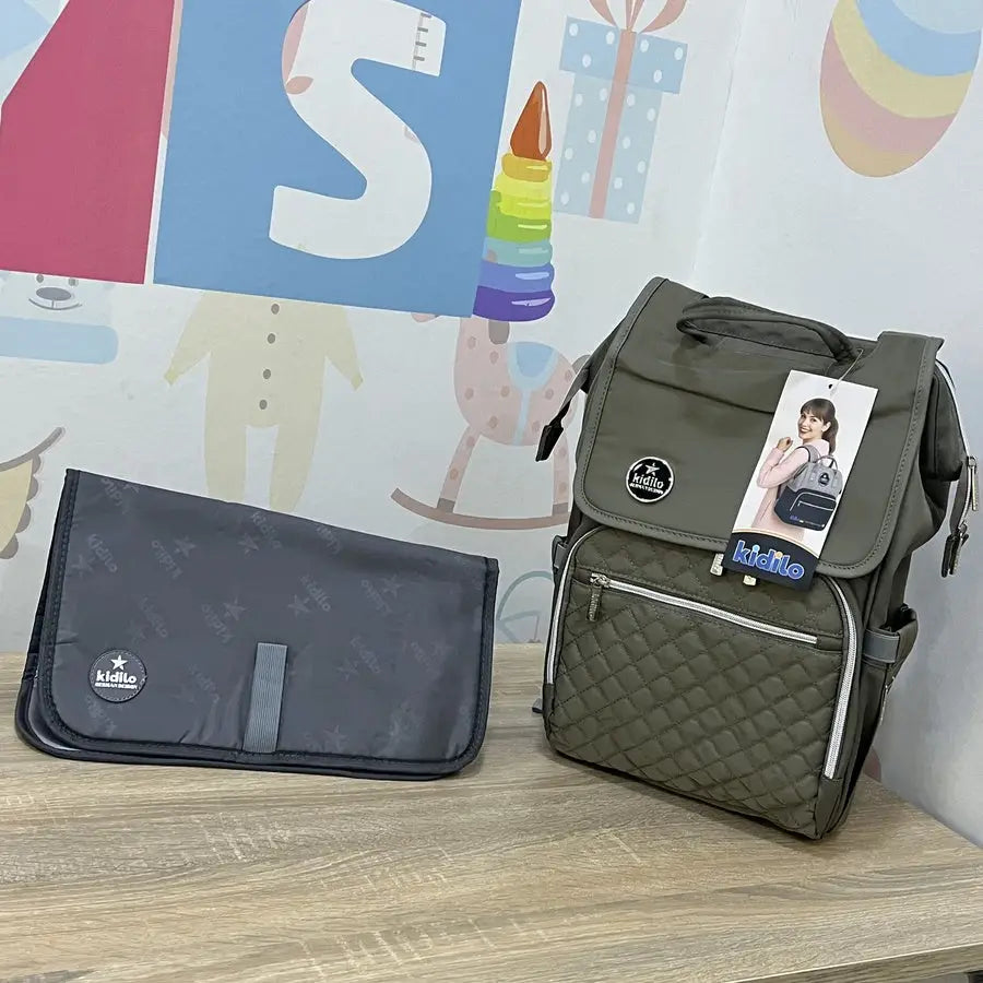 Kidilo X003: green bag with quilted pocket and changing mat against a patterned wall.