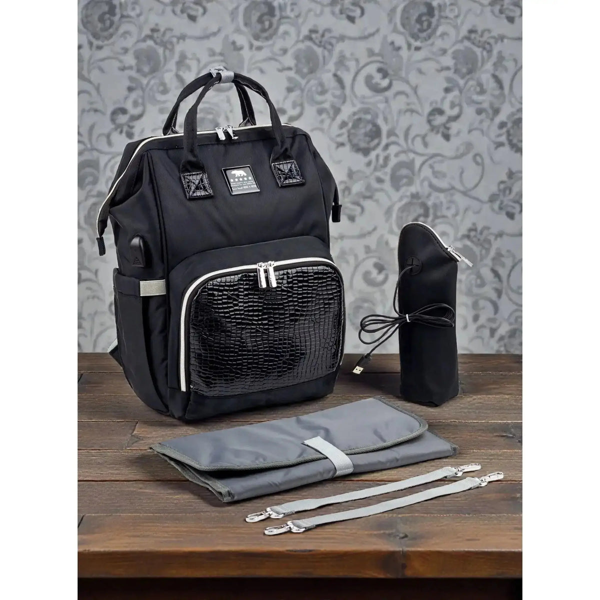Lucid diaper backpack – black backpack with bottle cover, mat and straps against a patterned wall