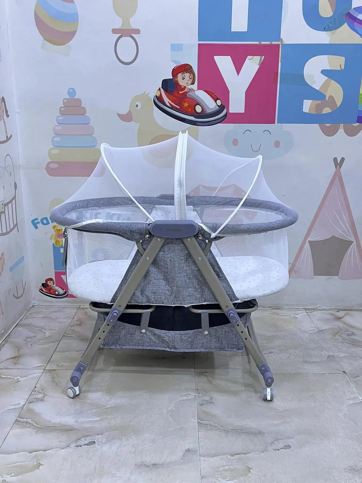 Nivorra NB-3F: grey bassinet side view with net raised on tiled showroom floor.