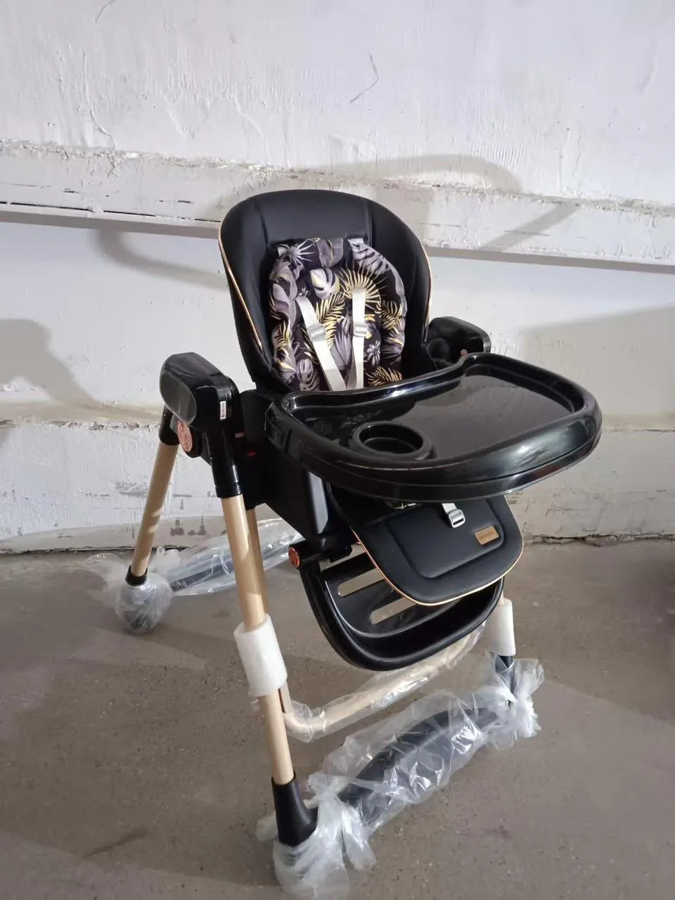 Umbrella X17 Pro: black high chair front angle with cup recess in tray and leaf-print cushion.